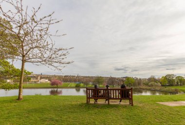 People sitting on bench watching  Inverleith Park pond, Edinburg clipart