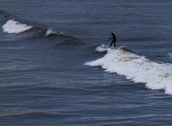 Surfer posiadających wiosło w kombinezon negocjowanie fale na być Tynemouth — Zdjęcie stockowe