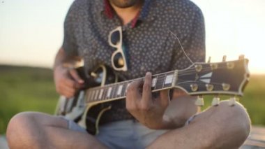 adam elektro gitar bir alanda gün batımında çalış.