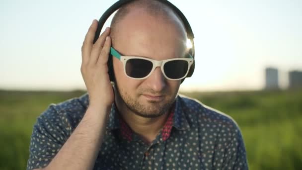 Man in headphones listening to music in a field at sunset — Stock Video