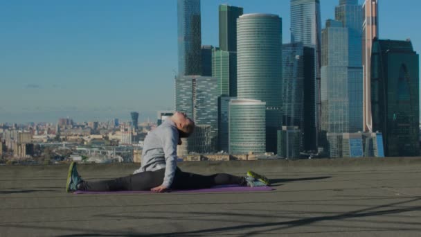 Girl stretching on the roof against the backdrop of the city — Stockvideo