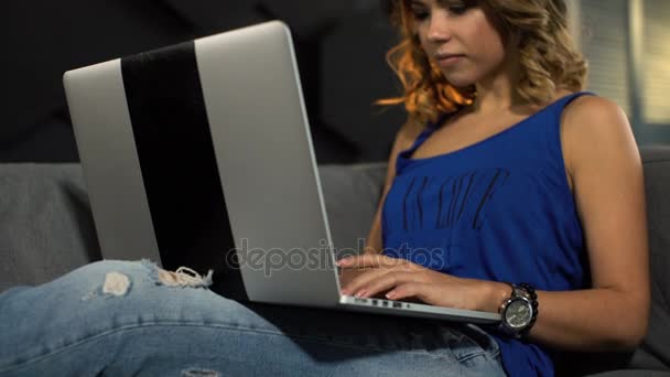 Mujer joven feliz con el ordenador portátil tumbado en el sofá en casa — Vídeos de Stock