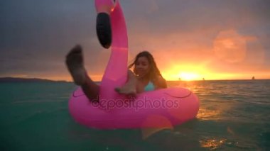 Güzel kız güzel bir gün batımı ile okyanusun ortasında şişme flamingo Yüzme