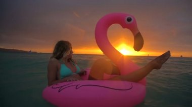 Güzel kız güzel bir gün batımı ile okyanusun ortasında şişme flamingo Yüzme