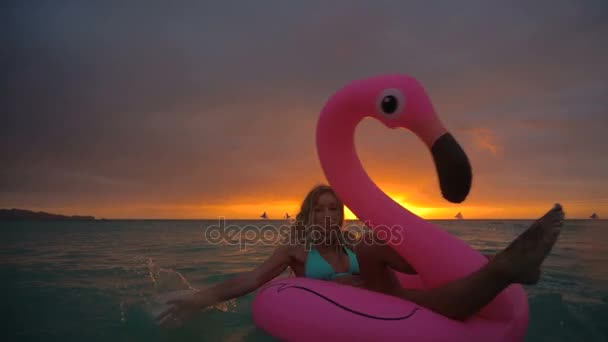 Menina bonita nadando flamingo inflável no meio do oceano com um pôr do sol bonito — Vídeo de Stock