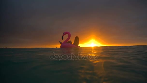 Belle fille nageant flamant rose gonflable au milieu de l'océan avec un beau coucher de soleil — Video