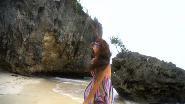 Young brunette girl in a bright dress runs along the white beach, smiling at the camera, developing hair. — Stock Video