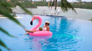 Hindistan cevizi içme ve pembe bir şişme şişme bir yüzme havuzunda - güzel model mükemmel şekiller egzotik bir tatil beldesine soğutma ile rahatlatıcı güzel genç kadın