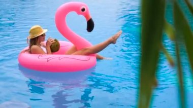 Hindistan cevizi içme ve pembe bir şişme şişme bir yüzme havuzunda - güzel model mükemmel şekiller egzotik bir tatil beldesine soğutma ile rahatlatıcı güzel genç kadın