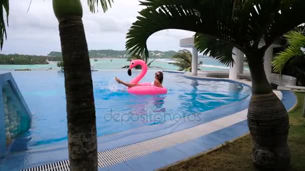 Schöne junge Frau, die Kokosnuss trinkt und es sich auf einer rosa aufblasbaren Matratze in einem Swimmingpool gemütlich macht - hübsches Modell mit perfekten Formen, die in einem exotischen Resort chillen — Stockvideo
