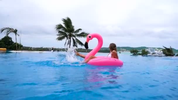 Schöne junge Frau, die Kokosnuss trinkt und es sich auf einer rosa aufblasbaren Matratze in einem Swimmingpool gemütlich macht - hübsches Modell mit perfekten Formen, die in einem exotischen Resort chillen — Stockvideo