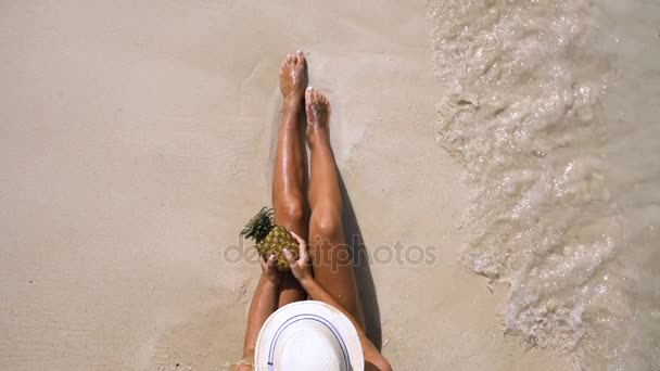 Sexig tjej i en hatt innehar en ananas på stranden med vågorna — Stockvideo