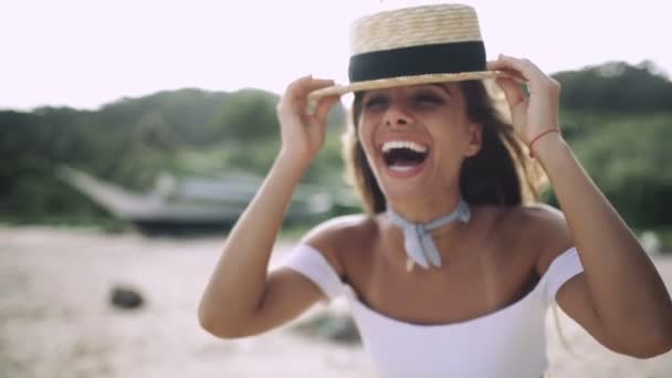 Sexy chica con una hermosa sonrisa en un sombrero riendo en la playa — Vídeos de Stock
