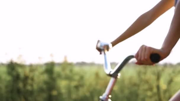 Ein junges blondes Mädchen in Hosen auf einem Retro-Fahrrad geht die Straße hinunter in das Feld — Stockvideo