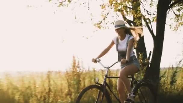 Uma jovem loira de calças na bicicleta retro descendo a estrada no campo — Vídeo de Stock