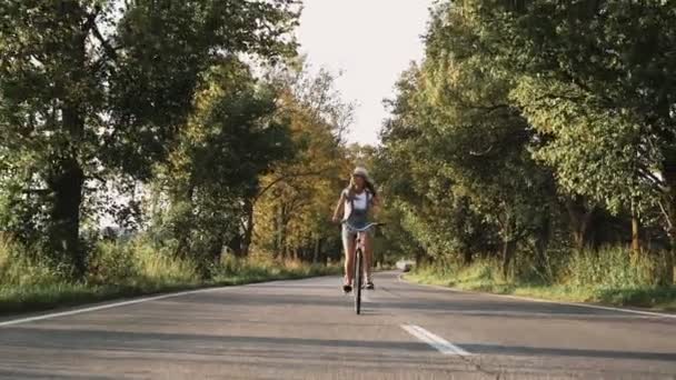 一个年轻的金发女孩在裤子上的复古自行车走在野外的道路 — 图库视频影像