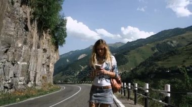 Genç sarışın turist kız etek dağlarda yolda yürüyor ve telefon arıyor