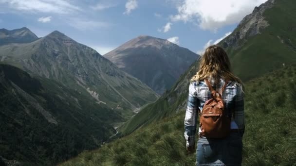 Ένα νεαρό κορίτσι σε μια φούστα με ένα σακίδιο πηγαίνει στην κορυφή των βουνών με τα όμορφα μαλλιά. Αργή κίνηση — Αρχείο Βίντεο