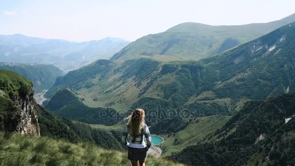Молодая девушка в юбке с рюкзаком идет на вершину гор с красивыми волосами. Медленное движение — стоковое видео