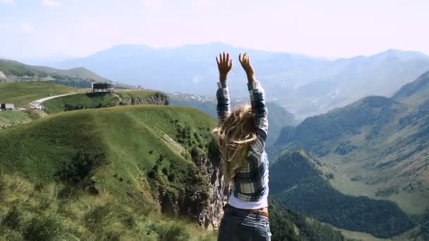 Una joven con una falda con una mochila va a la cima de las montañas con el pelo hermoso. Movimiento lento — Vídeos de Stock