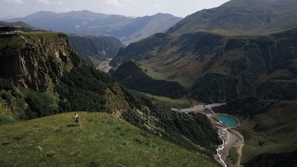 Aéreo - um voo sobre uma jovem que corre por aí se alegra nas montanhas com uma mochila. Sente felicidade e liberdade nas montanhas — Vídeo de Stock