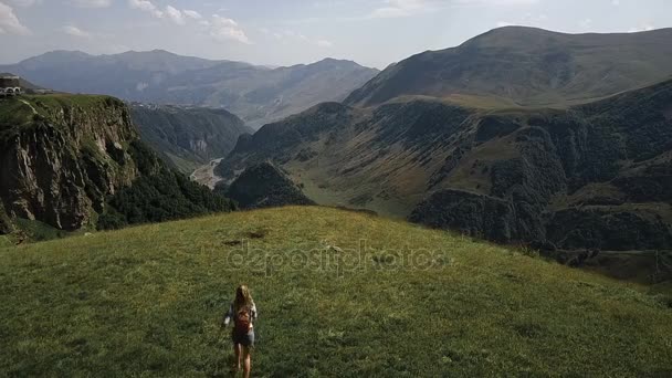 Εναέρια - μια πτήση πάνω από ένα νεαρό κορίτσι που τρέχει γύρω από χαίρεται στα βουνά με ένα σακίδιο. Αισθάνεται την ευτυχία και την ελευθερία στα βουνά — Αρχείο Βίντεο
