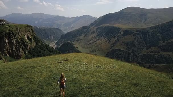 Aérea - un vuelo sobre una joven que corre alrededor se regocija en las montañas con una mochila. Siente felicidad y libertad en las montañas — Vídeos de Stock