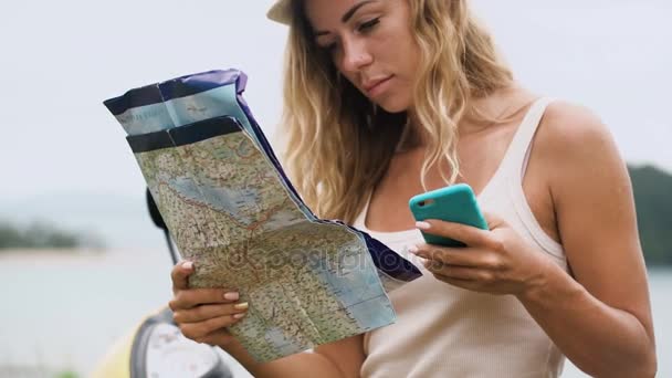 Blondes Mädchen mit Hut, sitzt auf dem Fahrrad und schaut auf Telefon und Karte, schaut auf die Route in Asien — Stockvideo