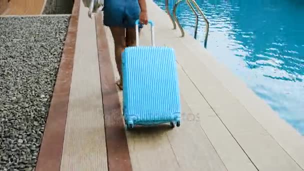 Mavi bir çanta ile tropikal bir otelde sarışın kız bir şapka ve tulum yerleşir. — Stok video
