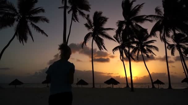 Het meisje loopt rond in de ochtend in de palmbomen bij dageraad — Stockvideo