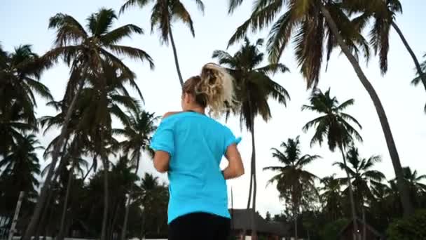La niña corre por la mañana en las palmeras al amanecer — Vídeo de stock