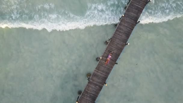 Aérea: la niña se encuentra en un puente de madera. Ondas en el fondo — Vídeo de stock