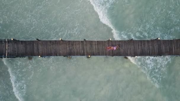 Aérea: la niña se encuentra en un puente de madera. Ondas en el fondo — Vídeos de Stock