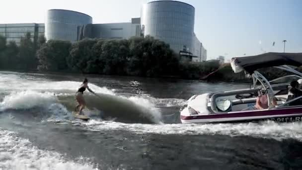 Jovem atleta europeia cavalgando wakesurf atrás de barco rebocando onda no rio — Vídeo de Stock
