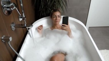 Evde, banyoda, rahatlamış kulaklıkla müzik dinleyen bir kız.