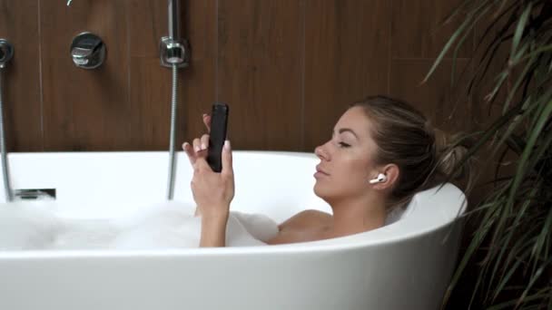 Ragazza a casa in bagno con relax ascolta musica sulle cuffie dal telefono — Video Stock