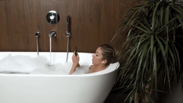 Ragazza a casa in bagno con relax ascolta musica sulle cuffie dal telefono — Video Stock