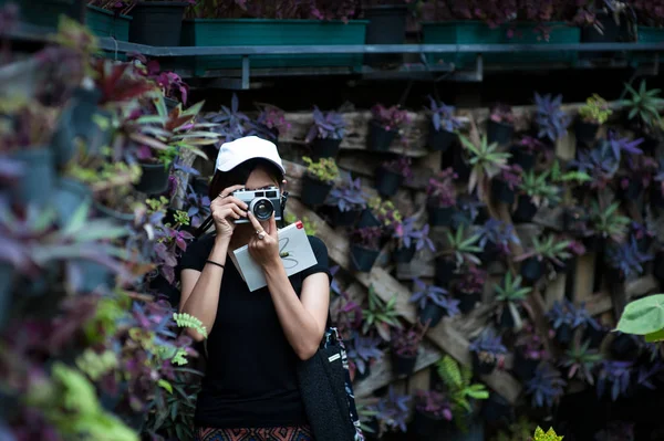 Hipster mujer tomando fotos con cámara de película retro en el jardín de flores del parque de la ciudad, hermosa chica fotografiada en la cámara vieja —  Fotos de Stock