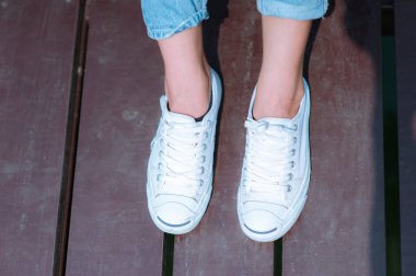 Beyaz ayakkabıları, kadının bacakları ile ahşap zemin üzerinde oturmuş spor ayakkabı moda