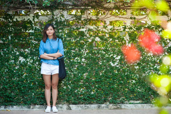 Γυναίκα, που χαμογελά ενώ ακουμπά στον τοίχο υπαίθρια, hipster ευτυχισμένη κομψή γυναίκα στέκεται στο τοίχο πράσινα φύλλα, καλοκαίρι ταξίδι έννοια — Φωτογραφία Αρχείου