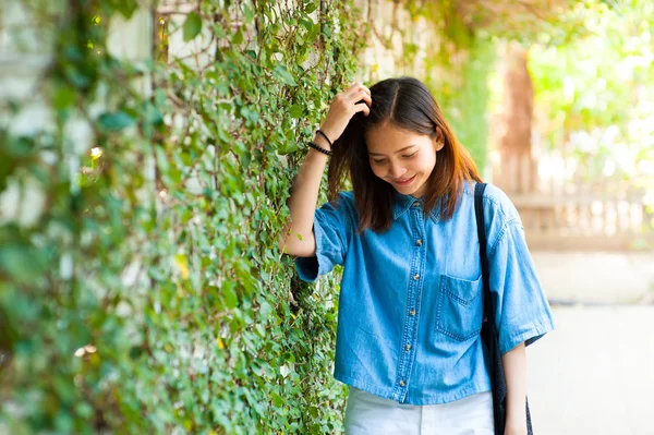 Mujer sonriendo mientras se apoya en la pared al aire libre, feliz mujer elegante hipster de pie en la pared de hojas verdes, concepto de viaje de verano —  Fotos de Stock