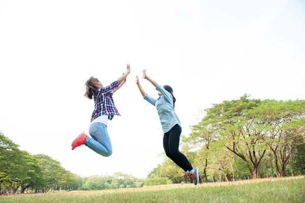 Due giovani donne felici che saltano sopra il cielo, saltando al parco estivo — Foto Stock