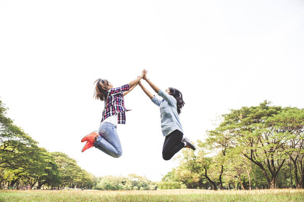 Две счастливые девушки прыгают по небу, прыгают в летнем парке
