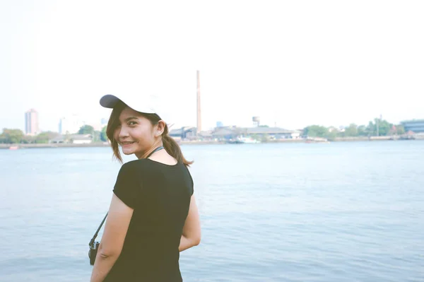 La mujer de pie en el lado del río y la joven sonriente sosteniendo la vieja cámara de fotos vintage —  Fotos de Stock