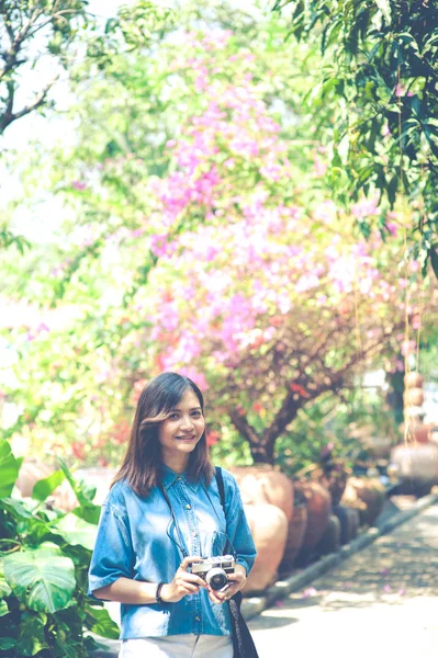 Hipster donna scattare foto con macchina fotografica retrò film nel giardino fiorito del parco della città, bella ragazza fotografata nella vecchia macchina fotografica — Foto Stock