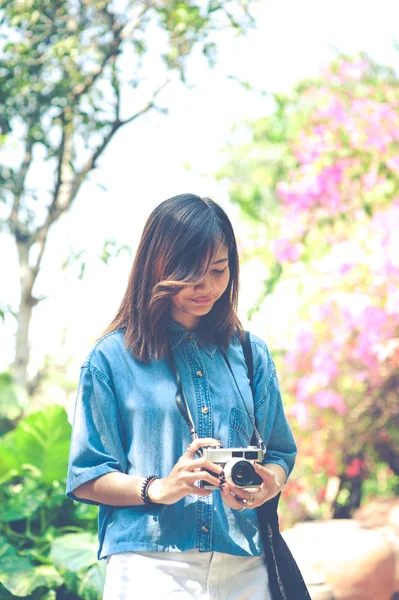 Hipster mujer tomando fotos con cámara de película retro en el jardín de flores del parque de la ciudad, hermosa chica fotografiada en la cámara vieja —  Fotos de Stock