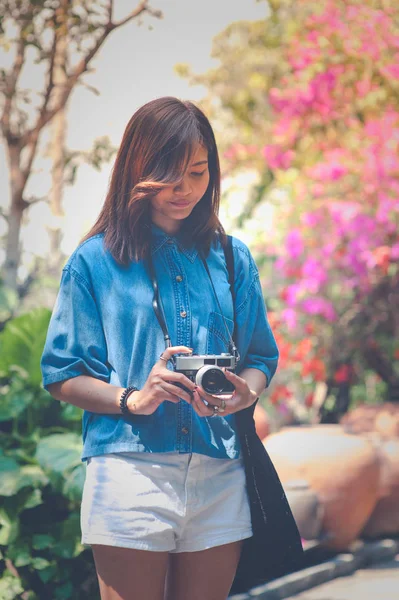 Hipster woman taking photos with retro film camera in flower garden of city park,beautiful girl photographed in the old camera — Stock Photo, Image