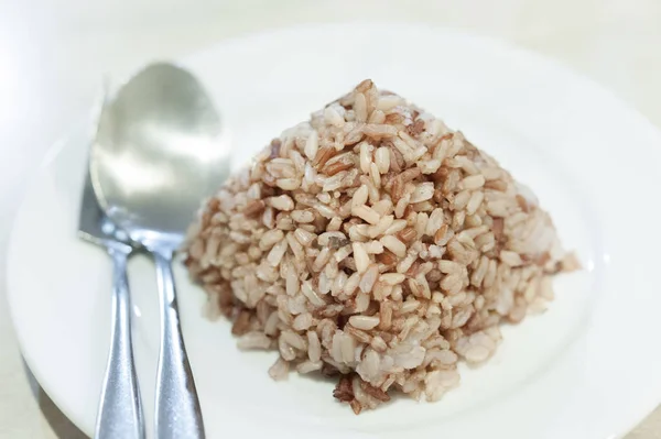 Arroz cozido marrom em um prato, colher ao lado; comida limpa; alimentação saudável . — Fotografia de Stock