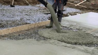 İşçiler inşaat alanında çalışıyor, zemin çalışıyor. Aile evinin temellerine beton dökme pompasının ayrıntıları. Beton karıştırma pompası temel plaka üzerinde çalışır, arkaplanda gökyüzü
