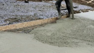 İşçiler inşaat alanında çalışıyor, zemin çalışıyor. Aile evinin temellerine beton dökme pompasının ayrıntıları. Beton karıştırma pompası temel plaka üzerinde çalışır, arkaplanda gökyüzü
